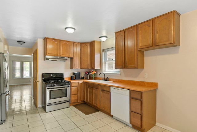 kitchen with a sink, brown cabinets, stainless steel appliances, under cabinet range hood, and light countertops