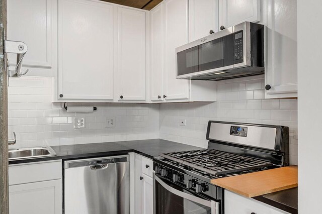 kitchen with dark countertops, white cabinets, decorative backsplash, and appliances with stainless steel finishes