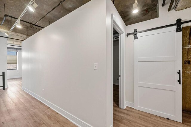 corridor featuring baseboards, a barn door, and light wood finished floors