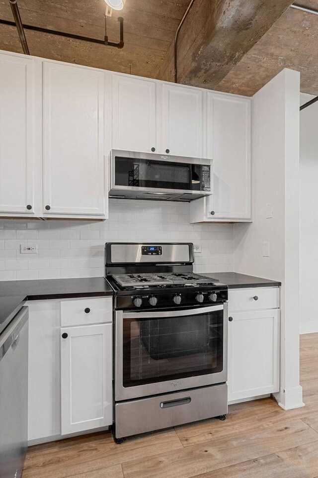kitchen with light wood finished floors, dark countertops, and stainless steel appliances