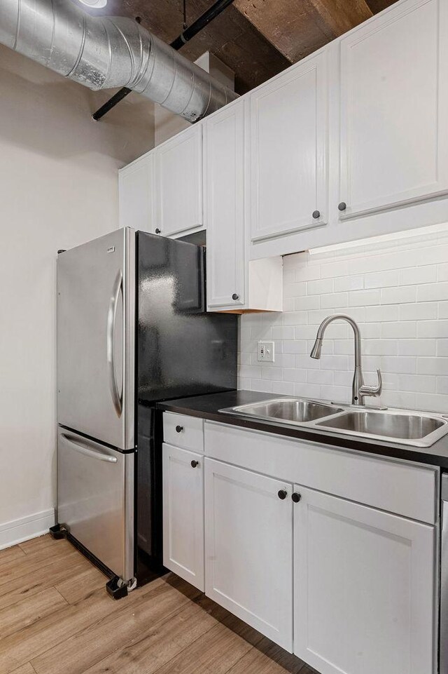 kitchen with light wood-type flooring, decorative backsplash, a sink, freestanding refrigerator, and white cabinets