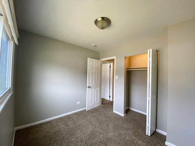 unfurnished bedroom with baseboards, a closet, and dark carpet