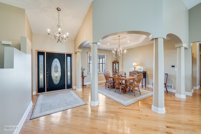 foyer entrance featuring ornate columns, a tray ceiling, wood finished floors, and an inviting chandelier