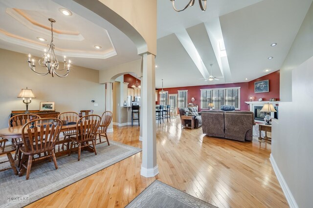 dining area featuring a tray ceiling, decorative columns, light wood-type flooring, baseboards, and arched walkways