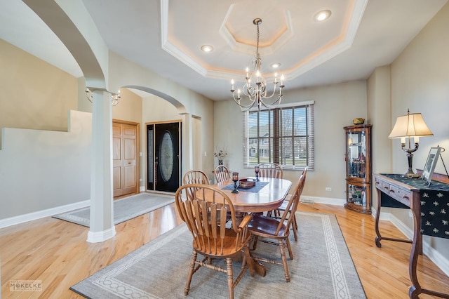 dining area featuring a raised ceiling, light wood-type flooring, baseboards, arched walkways, and an inviting chandelier