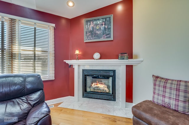 living area featuring visible vents, baseboards, a fireplace, wood finished floors, and vaulted ceiling