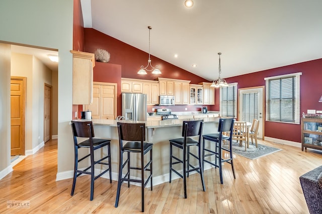 kitchen with glass insert cabinets, a kitchen bar, light wood-type flooring, and appliances with stainless steel finishes