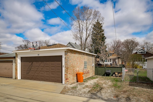 view of side of property with driveway, brick siding, an outbuilding, a garage, and fence