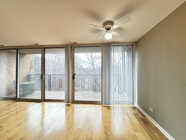 interior space with ceiling fan, visible vents, wood finished floors, and a wall of windows