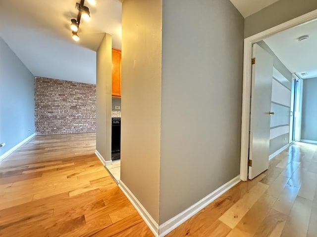 hallway featuring light wood-style flooring, brick wall, and baseboards
