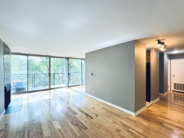 spare room featuring light wood finished floors, baseboards, a wall of windows, and visible vents