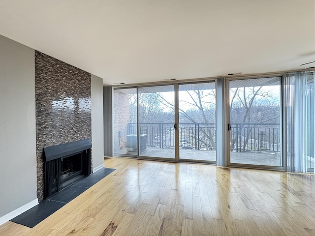 unfurnished living room featuring floor to ceiling windows, a large fireplace, baseboards, and wood finished floors