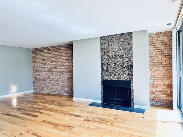 unfurnished living room with a tiled fireplace, brick wall, wood finished floors, and baseboards