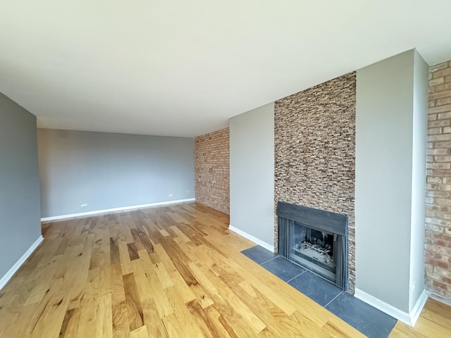 unfurnished living room featuring a fireplace with flush hearth, wood finished floors, and baseboards