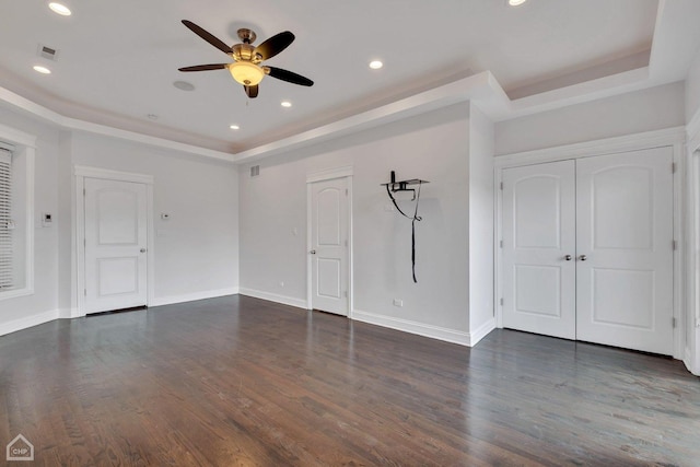 empty room featuring a ceiling fan, visible vents, dark wood-style flooring, a raised ceiling, and baseboards