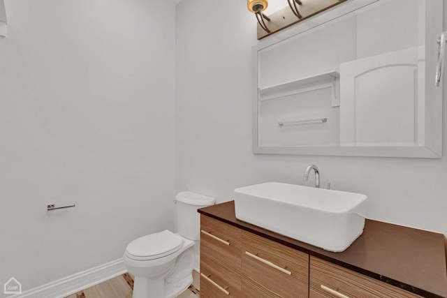 half bath with toilet, wood finished floors, vanity, and baseboards