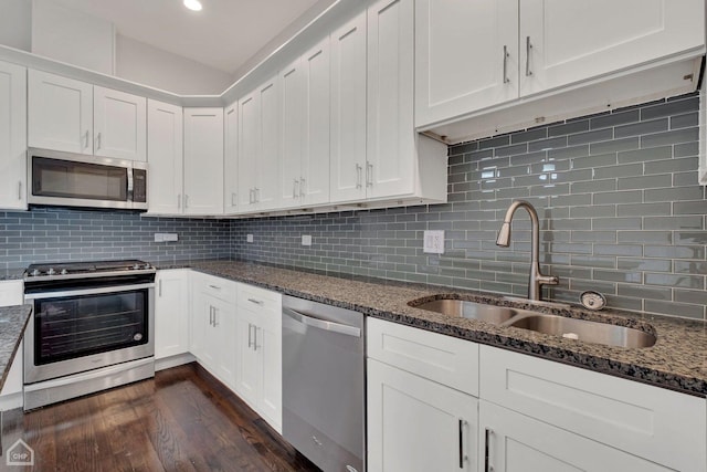 kitchen with a sink, dark wood finished floors, dark stone counters, stainless steel appliances, and backsplash