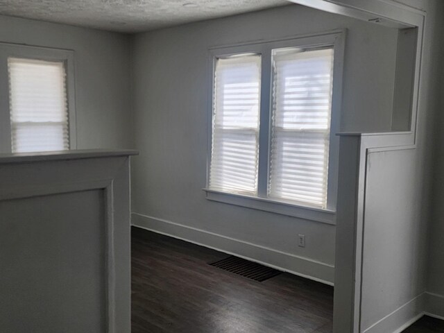 empty room featuring plenty of natural light, dark wood-style floors, baseboards, and visible vents