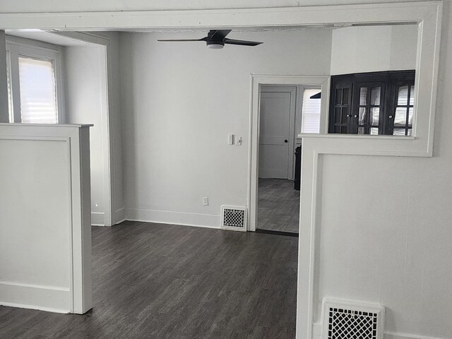 empty room with a ceiling fan, dark wood-type flooring, baseboards, and visible vents