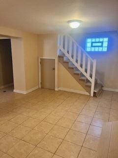 below grade area with light tile patterned flooring, stairs, and baseboards