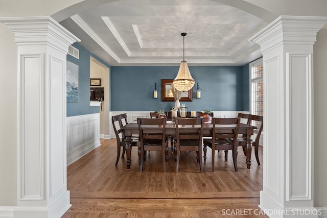 dining space featuring decorative columns, arched walkways, wainscoting, and a raised ceiling