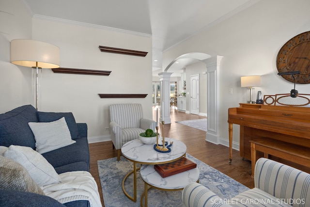 living area with decorative columns, ornamental molding, baseboards, arched walkways, and wood finished floors