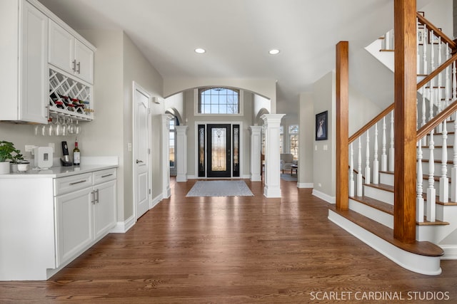 foyer entrance with recessed lighting, ornate columns, dark wood finished floors, arched walkways, and a dry bar