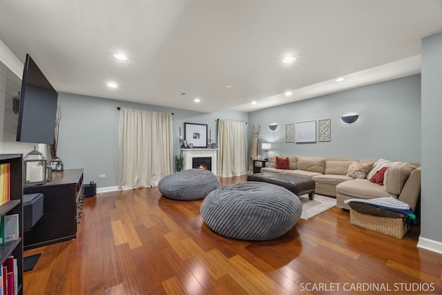 living room with a warm lit fireplace, baseboards, wood finished floors, and recessed lighting