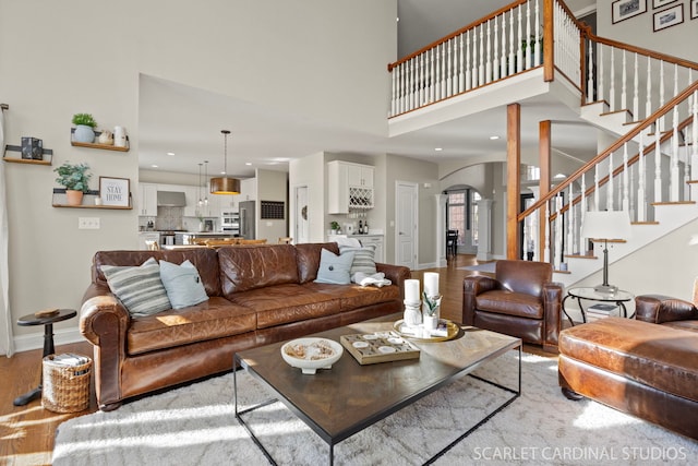 living area with arched walkways, a towering ceiling, light wood-style flooring, and stairway