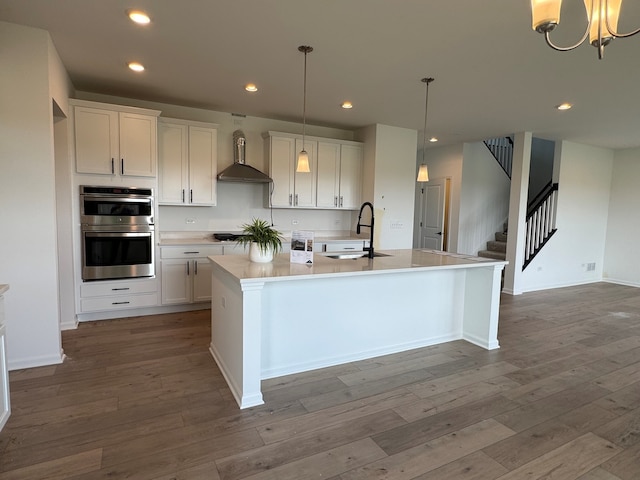 627 Henry Ln, Oswego, IL 60543 - kitchen with wall chimney exhaust hood, double oven, an island with sink, wood finished floors, and white cabinetry