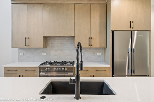 kitchen featuring light brown cabinetry, premium appliances, light countertops, a sink, and decorative backsplash