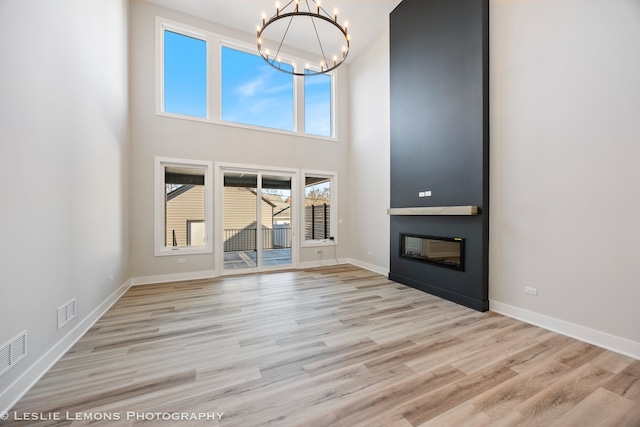 unfurnished living room with wood finished floors, a towering ceiling, a large fireplace, and a notable chandelier