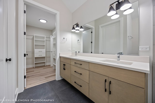 bathroom featuring a walk in closet, double vanity, baseboards, and a sink