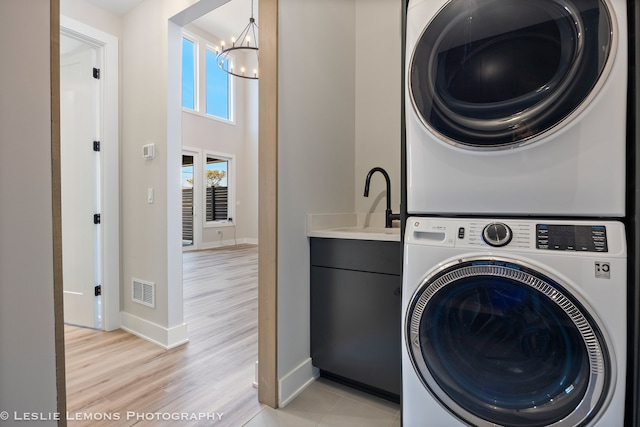 clothes washing area featuring visible vents, stacked washing maching and dryer, baseboards, cabinet space, and a notable chandelier