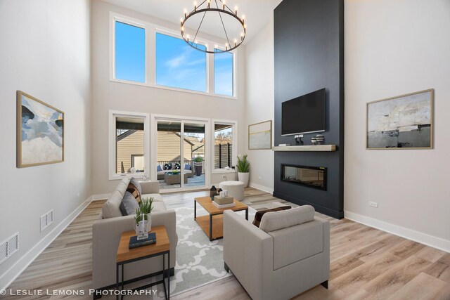 living area featuring a high ceiling, a glass covered fireplace, wood finished floors, and an inviting chandelier