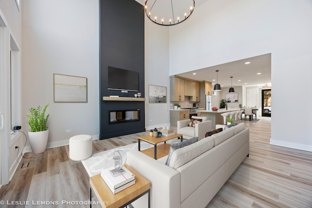 living room with light wood-style floors, an inviting chandelier, a towering ceiling, baseboards, and recessed lighting