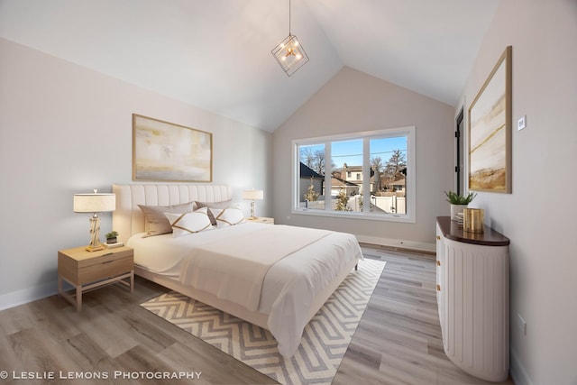 bedroom with vaulted ceiling, baseboards, and light wood-style floors