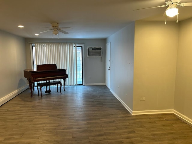 living area with dark wood-style floors, an AC wall unit, ceiling fan, and baseboards