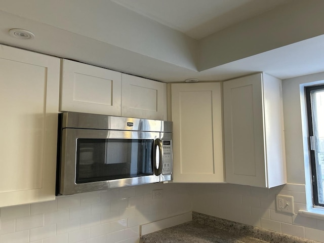 details with white cabinets, stainless steel microwave, and backsplash
