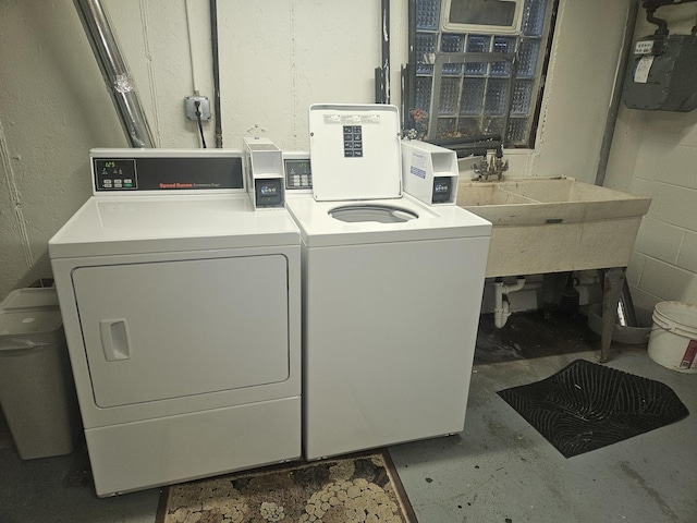 washroom with concrete block wall, a sink, and washer and dryer