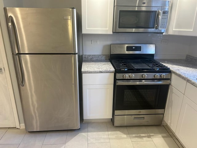 kitchen with light tile patterned flooring, white cabinets, light stone countertops, tasteful backsplash, and appliances with stainless steel finishes
