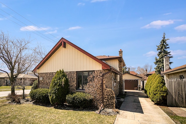 view of home's exterior with a chimney, fence, an outdoor structure, brick siding, and a detached garage
