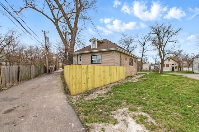 view of side of home featuring brick siding, fence, aphalt driveway, and a lawn