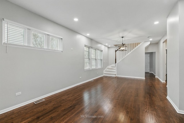 unfurnished room featuring dark wood-style flooring, visible vents, baseboards, and stairs
