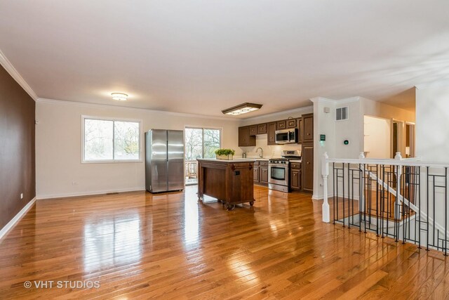 kitchen featuring a center island, crown molding, a sink, light wood-style floors, and appliances with stainless steel finishes
