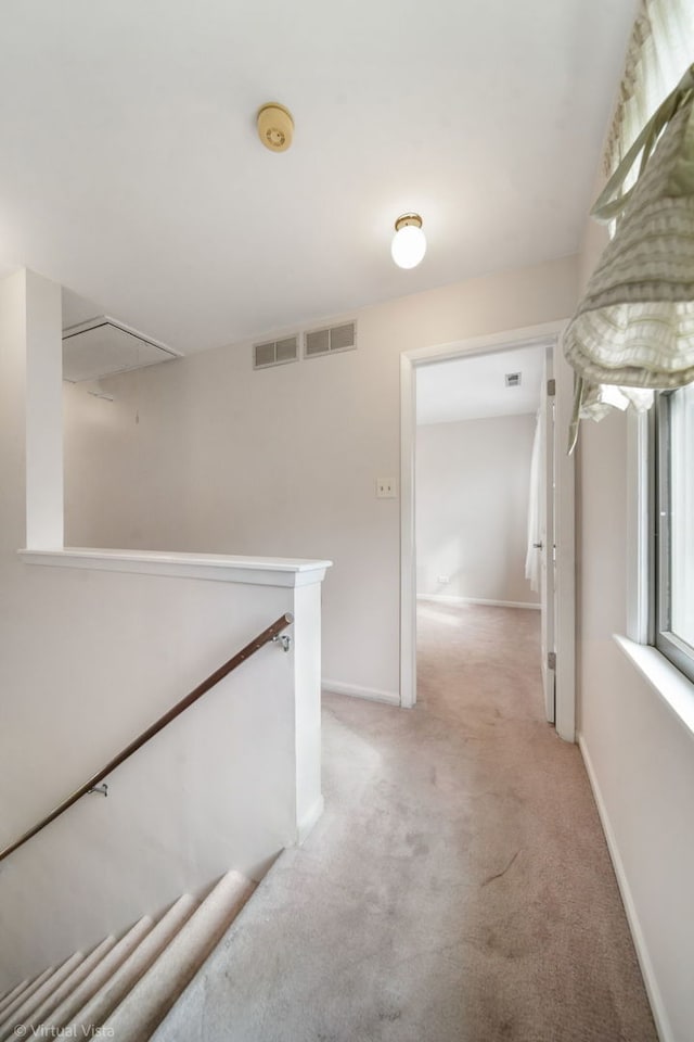 corridor with visible vents, baseboards, attic access, and light carpet