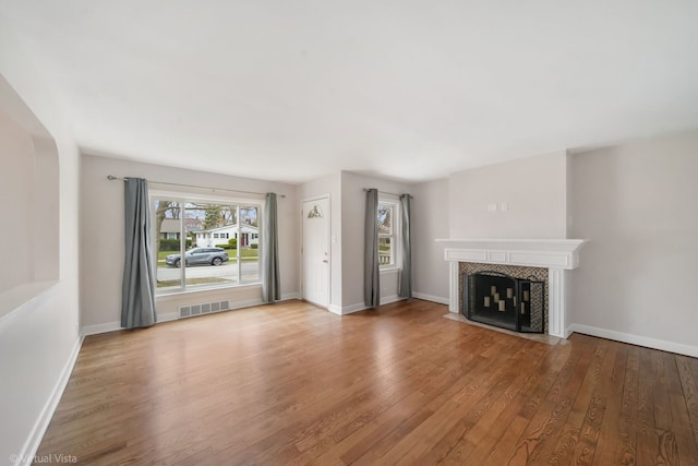 unfurnished living room featuring visible vents, baseboards, a tile fireplace, and wood finished floors