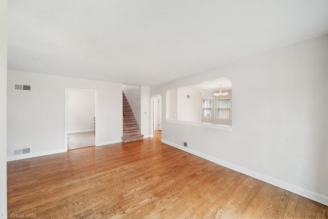 unfurnished living room featuring visible vents, light wood-type flooring, a notable chandelier, and stairway