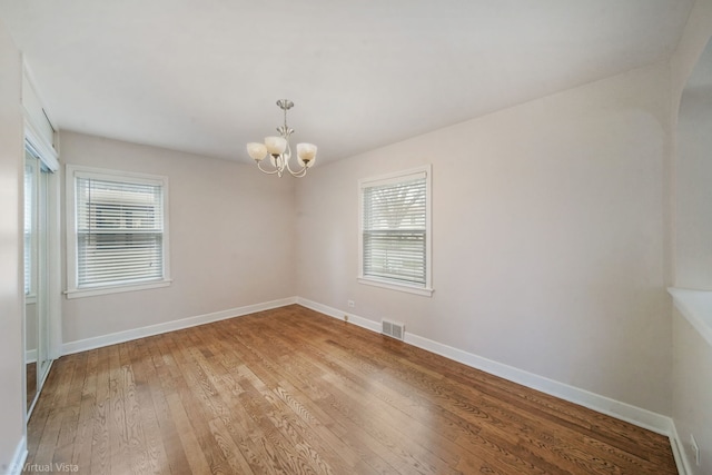 unfurnished room featuring baseboards, wood-type flooring, a notable chandelier, and visible vents