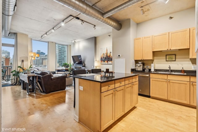 kitchen with dark countertops, a kitchen island, light brown cabinets, light wood-type flooring, and stainless steel dishwasher
